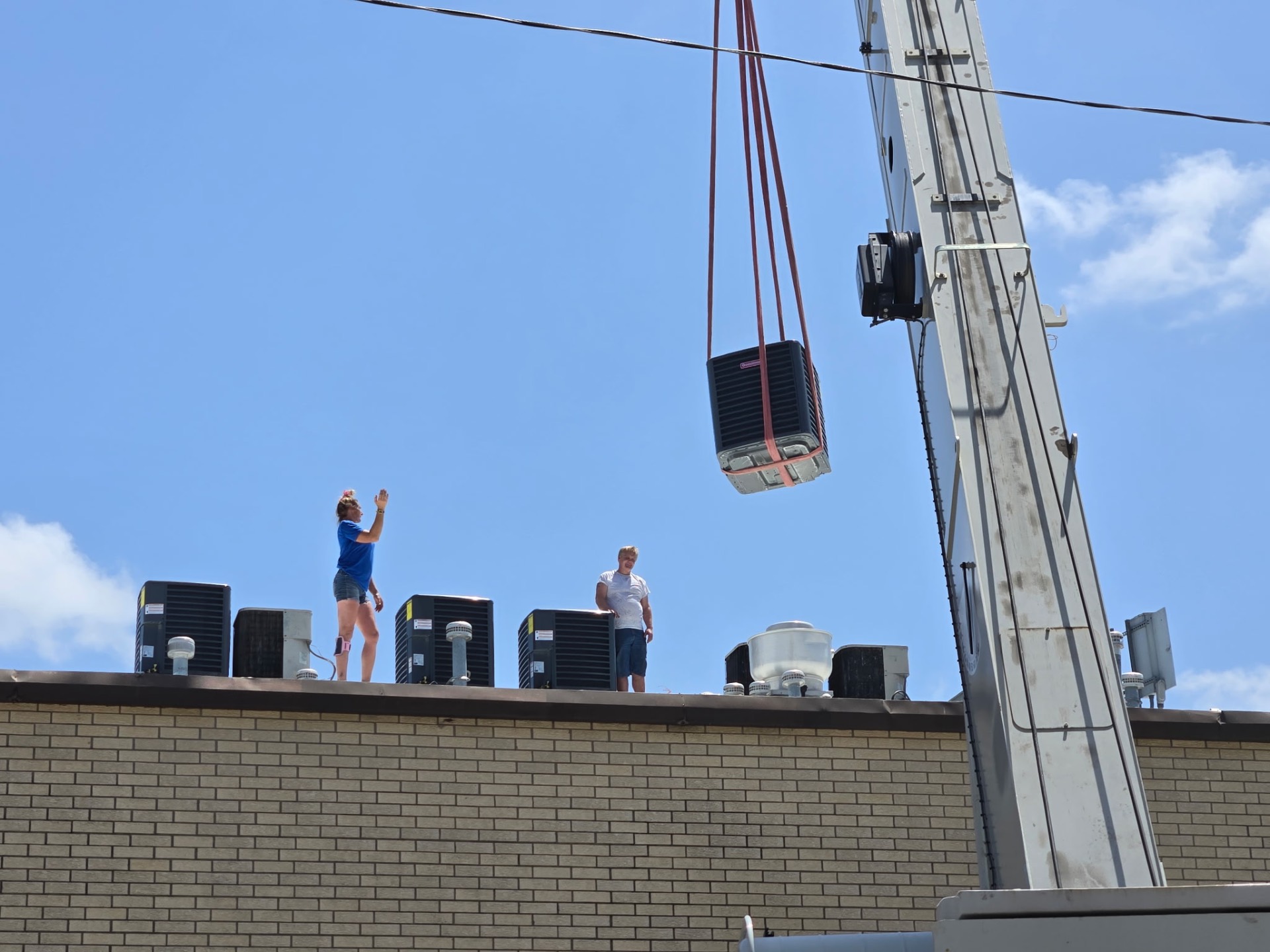 Crane lifting new commercial rooftop HVAC unit into place