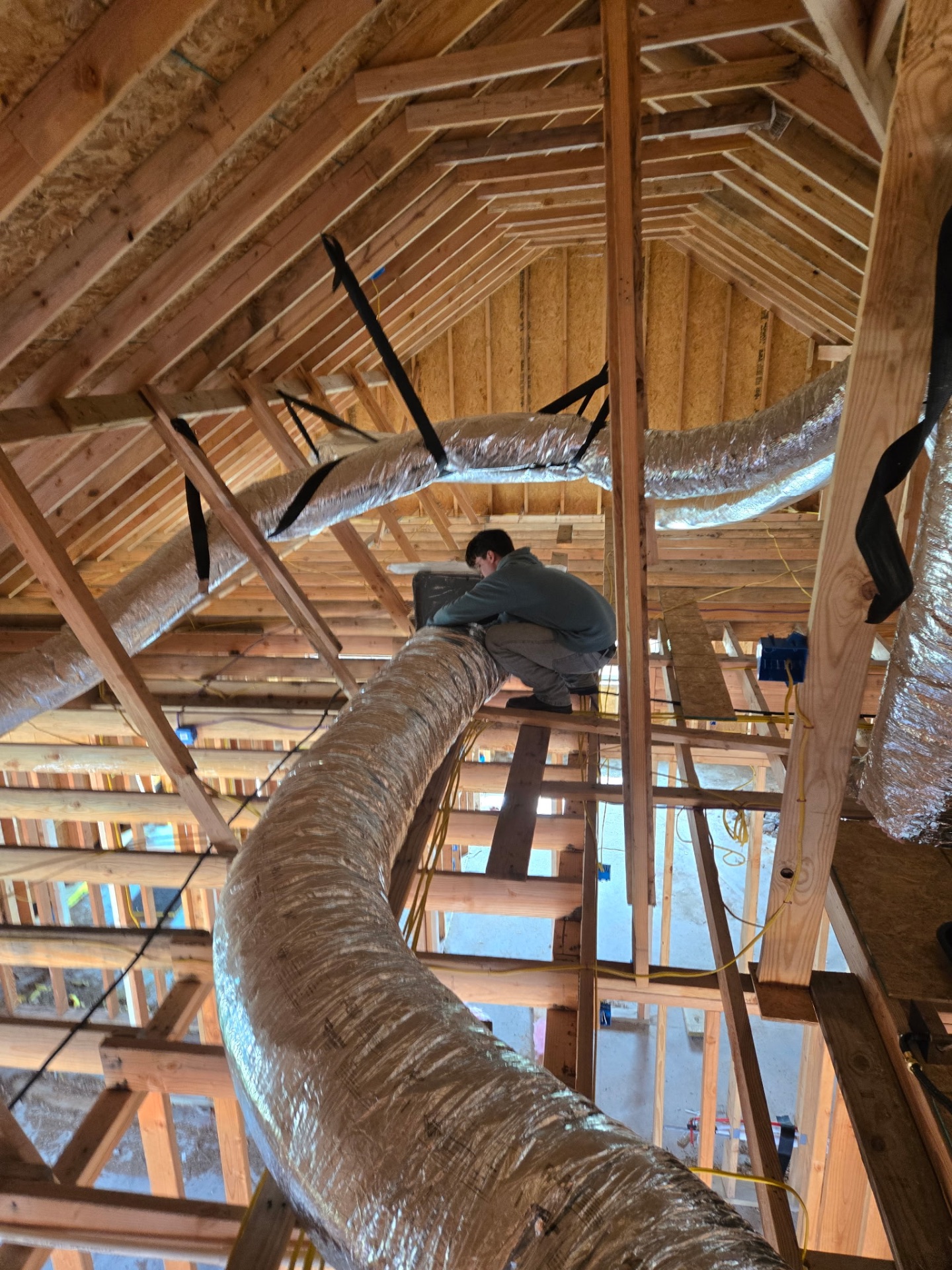Kingdom Heat & Air technician installing ductwork in new construction attic